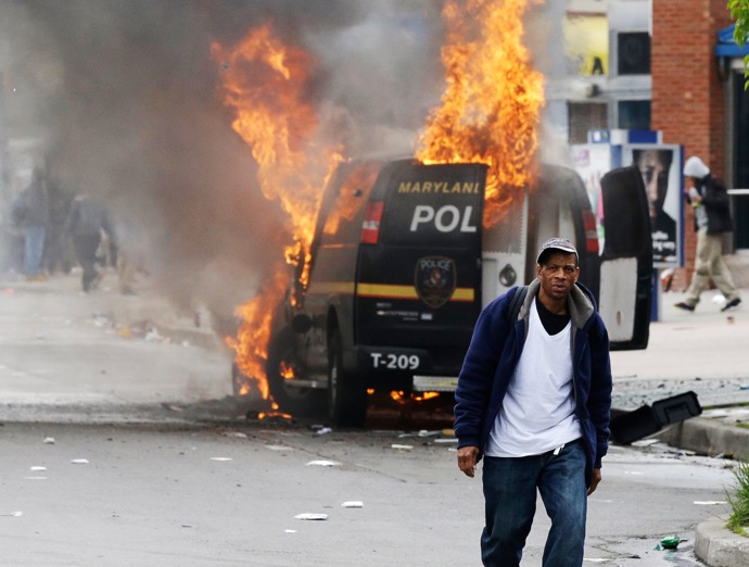 Image: A man walks past a burning police vehicle